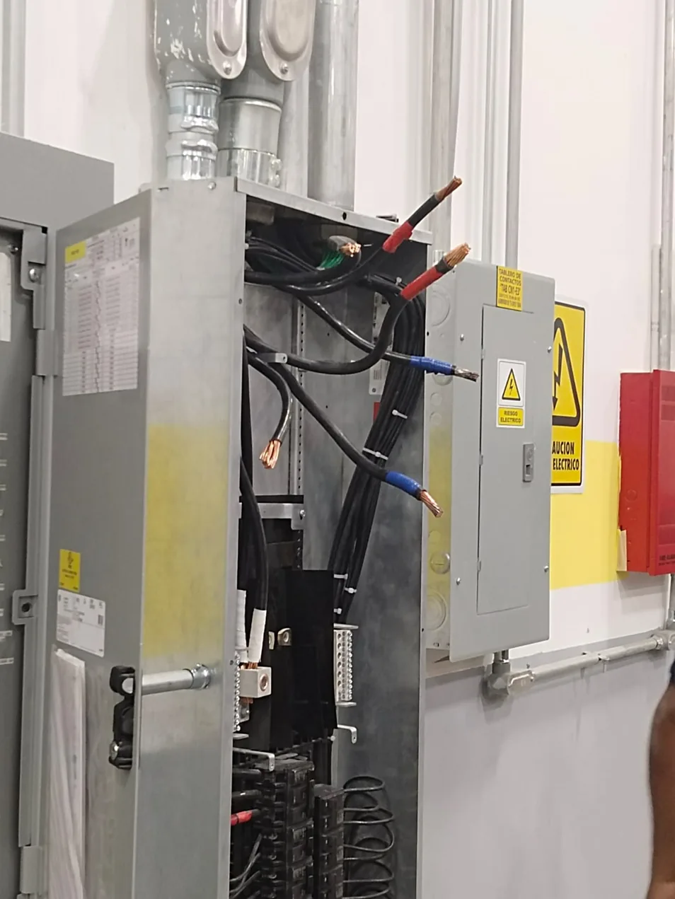 Tablero de distribución eléctrica industrial abierto durante un mantenimiento, con señalización de seguridad